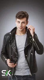 Front studio portrait of a model wearing our handcrafted men's black genuine leather biker jacket with ribbed sleeve padding, wide lapels, and asymmetrical metal zippers.
