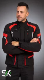 Front studio portrait of a male model with arms crossed wearing a black textile motorcycle jacket with red shoulder accents and zippered chest air vents.