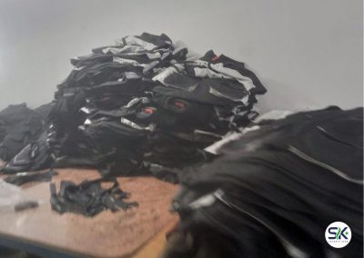 A large stack of completed black and grey technical jackets staged for final inspection and packaging at the SK Jackets Star manufacturing facility.