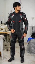 Model wearing a black, grey, and red Cordura biker suit with armor sliders in a manufacturing facility.