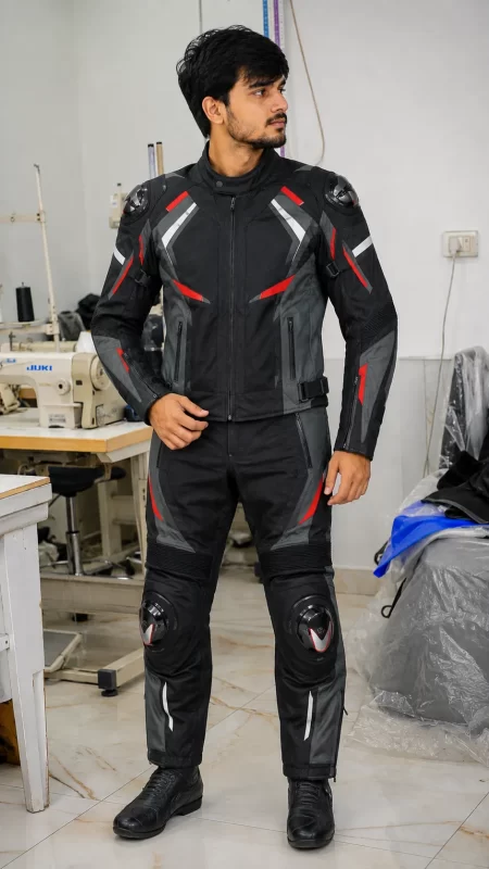 Model wearing a black, grey, and red Cordura biker suit with armor sliders in a manufacturing facility.