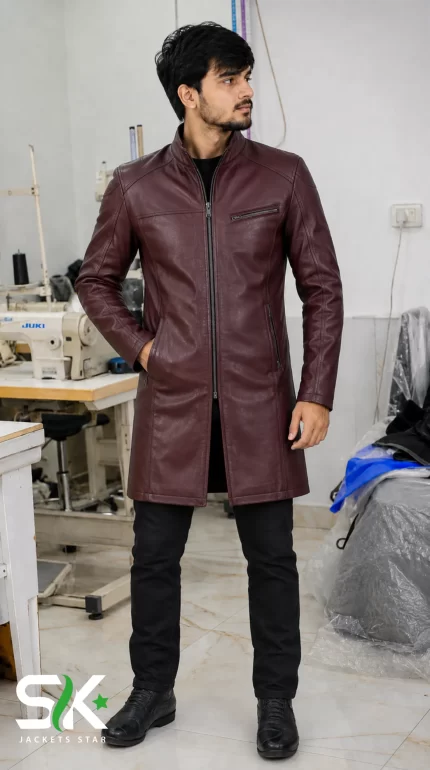 Front view of a male model wearing our manufactured longline maroon leather coat with stand collar, exposed central zipper, and chest zip pocket inside our stitching facility.