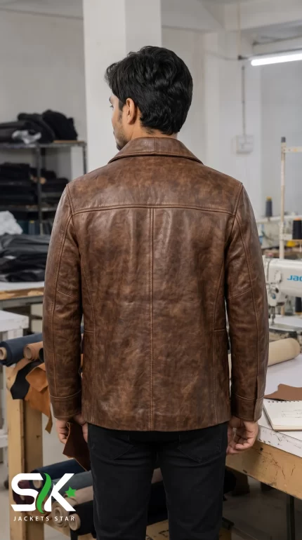 Rear perspective of a male model wearing our manufactured distressed brown leather safari field jacket inside our apparel production factory.