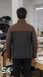Back view of a male model wearing our custom manufactured brown and black softshell jacket inside our apparel factory.