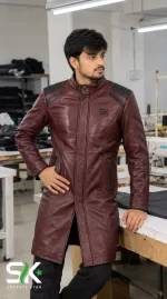 Front view of a male model wearing our custom manufactured longline maroon leather trench coat with black padded shoulders and stand collar inside our workshop.