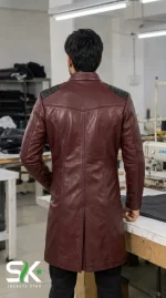 Rear perspective of a male model wearing our manufactured maroon longline leather coat with shoulder padding and a center back vent inside our workshop.