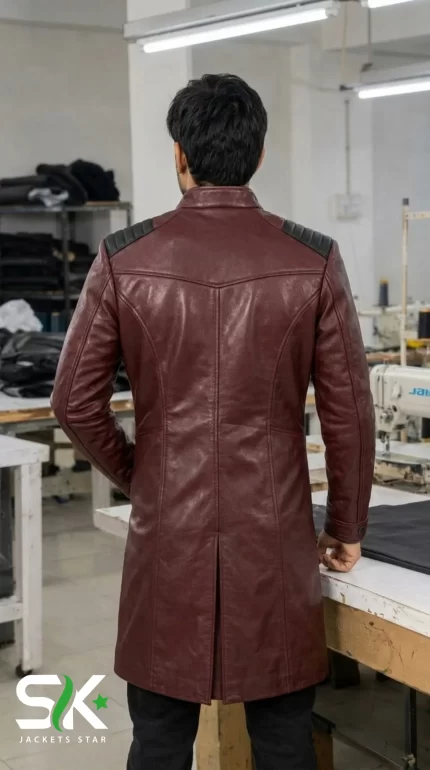 Rear perspective of a male model wearing our manufactured maroon longline leather coat with shoulder padding and a center back vent inside our workshop.