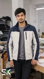 Front view of a male model wearing a two-tone navy blue and off-white softshell jacket in a factory environment.