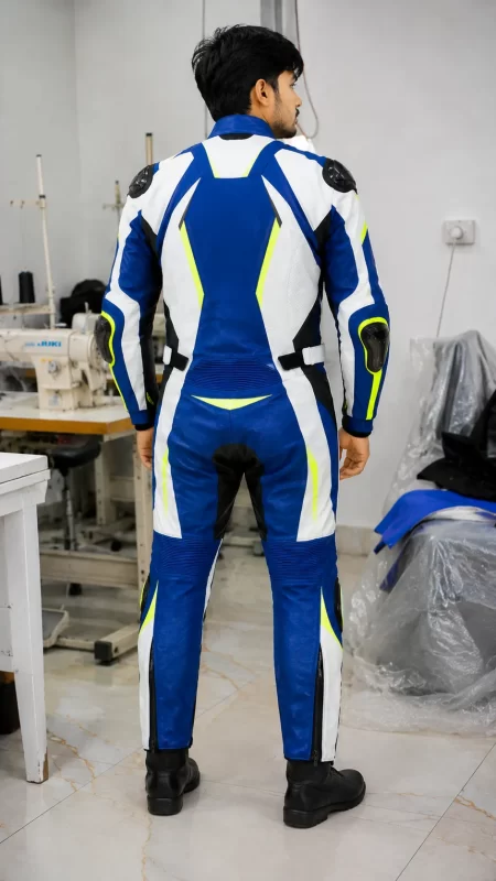 Rear view of a model wearing a blue, white, black, and neon yellow leather motorcycle racing suit with aerodynamic speed hump in a factory setting.
