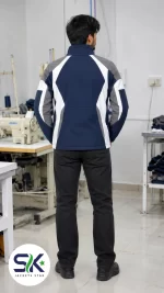 Rear view of model wearing navy blue grey and white windproof softshell jacket inside Sialkot garment manufacturing factory.