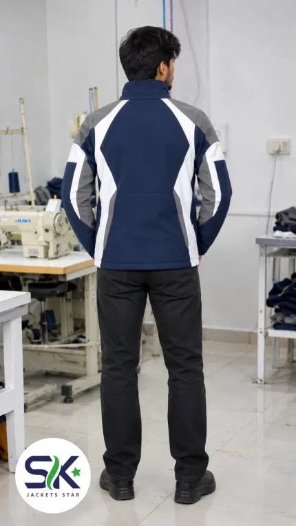 Rear view of model wearing navy blue grey and white windproof softshell jacket inside Sialkot garment manufacturing factory.
