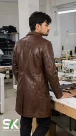 Three-quarter back view of a male model wearing our custom manufactured brown leather car coat with a structured upper yoke inside our garment production facility.